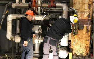 Two men fixing industrial plumbing equipment